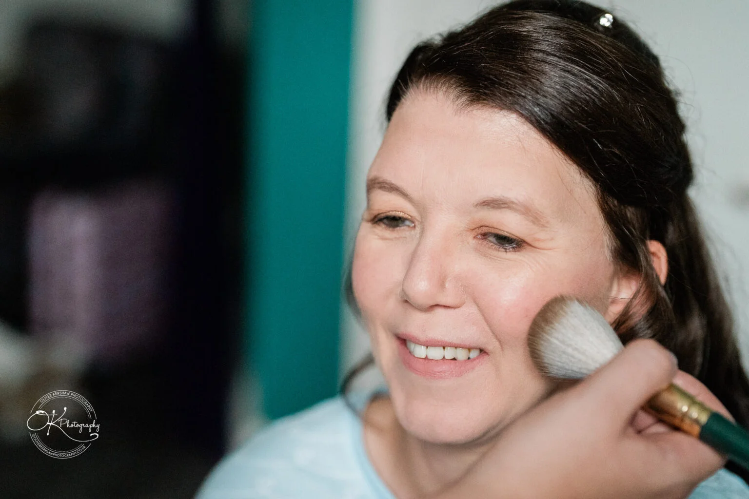 Makeney Hall Hotel - Wedding Photography A woman smiling while having makeup applied with a brush.