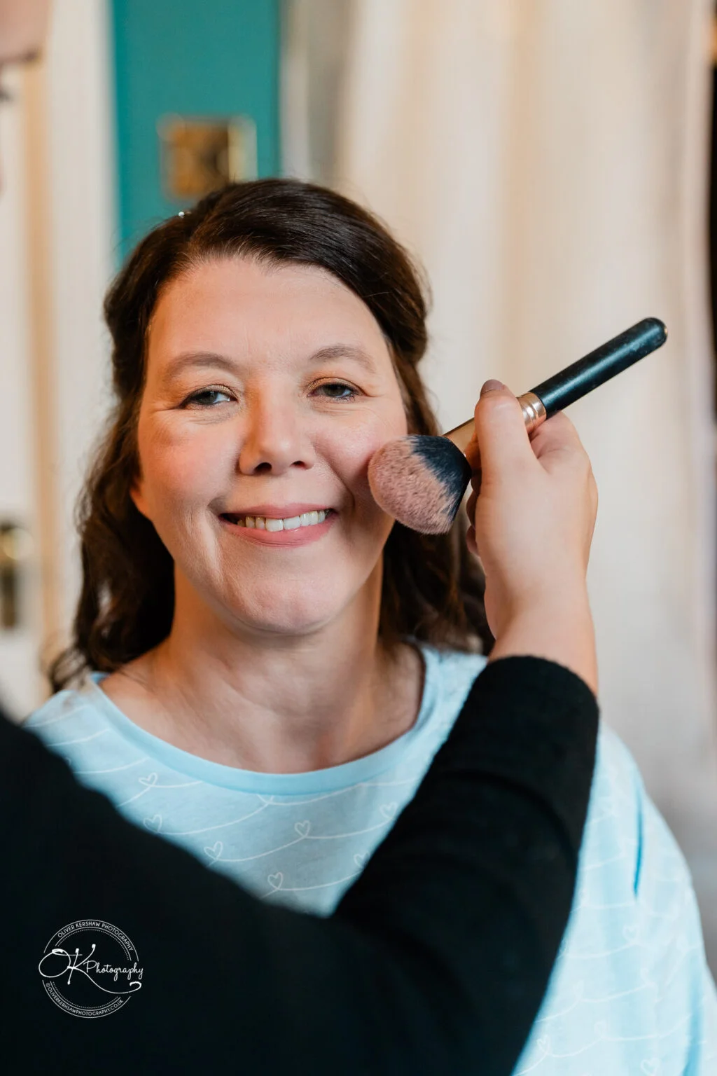 Makeney Hall Hotel - Wedding Photography A woman smiling while having makeup applied with a brush.