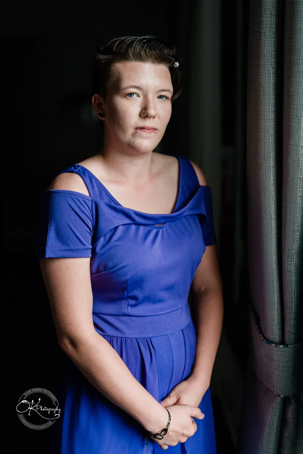 Makeney Hall Hotel - Wedding Photography Person in a purple dress standing by a window with dark curtains.