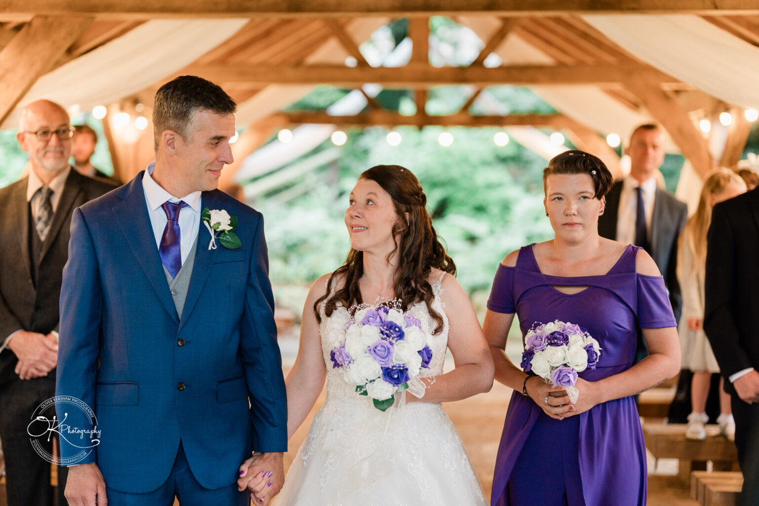 A bride and groom holding hands, standing with a bridesmaid during a wedding ceremony at Makeney Hall Hotel.