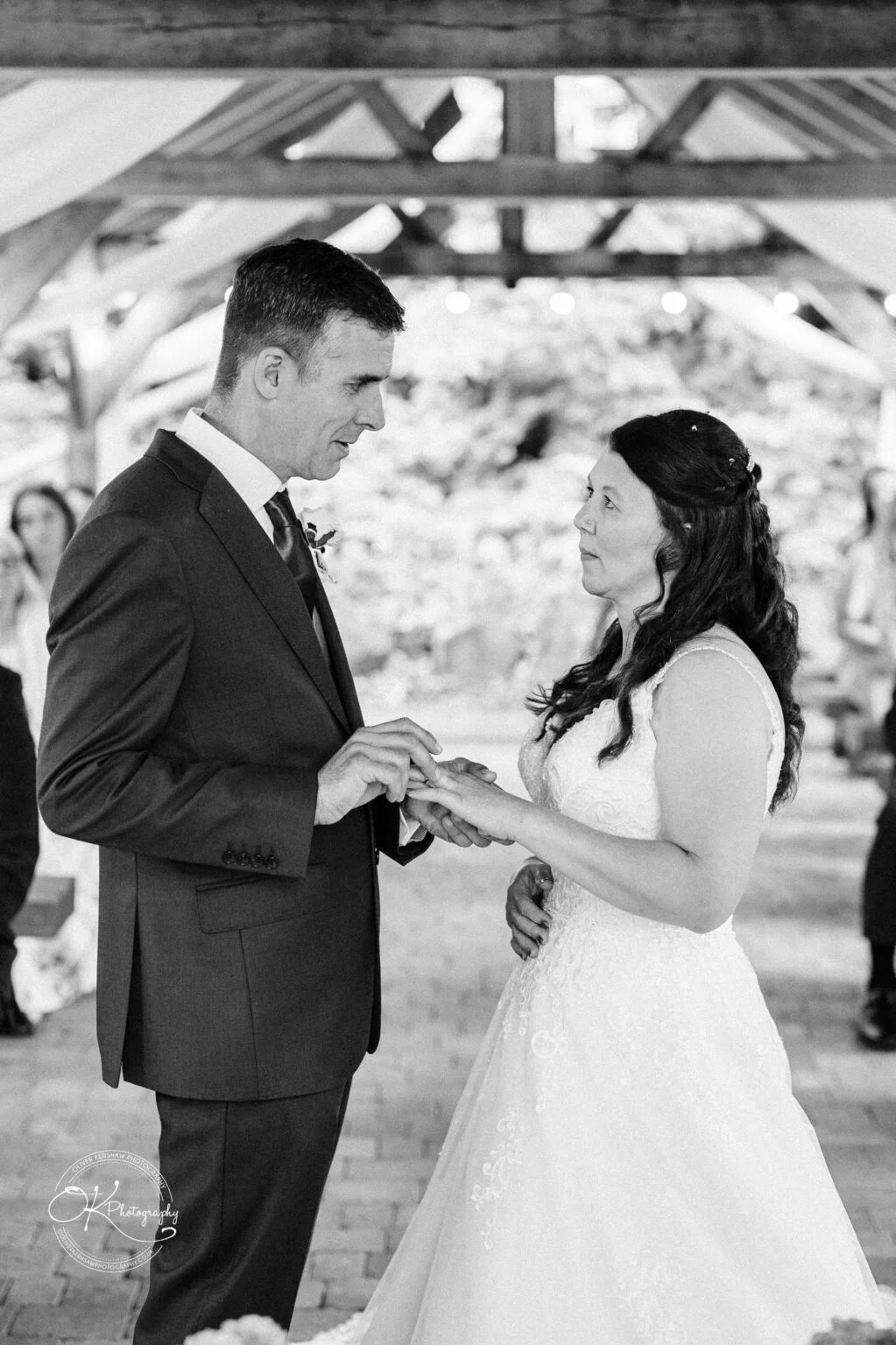 Makeney Hall Hotel - Wedding Photography A bride and groom exchange rings during their wedding ceremony under a wooden pergola.