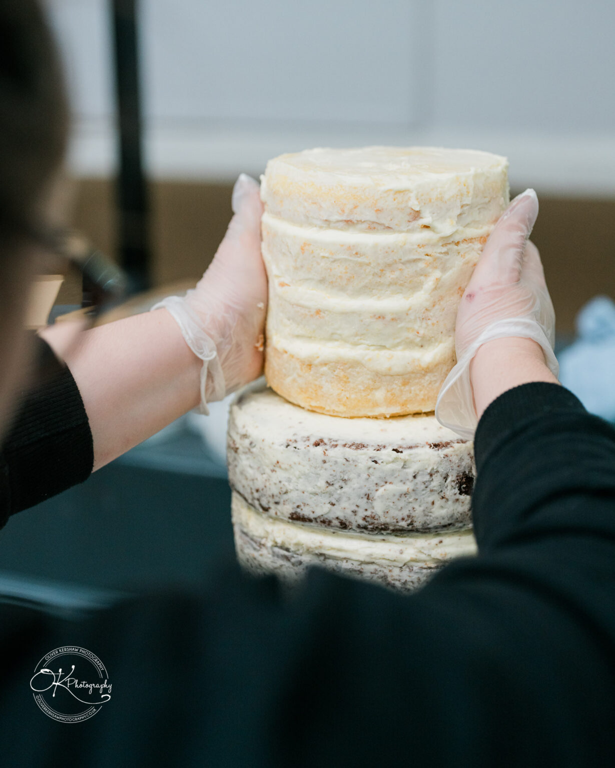 Hands with gloves stacking layers of a naked cake.