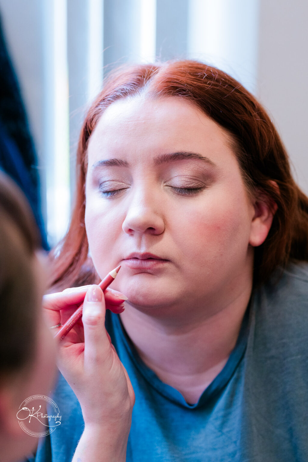 A woman with closed eyes having her makeup applied with a red lip liner.