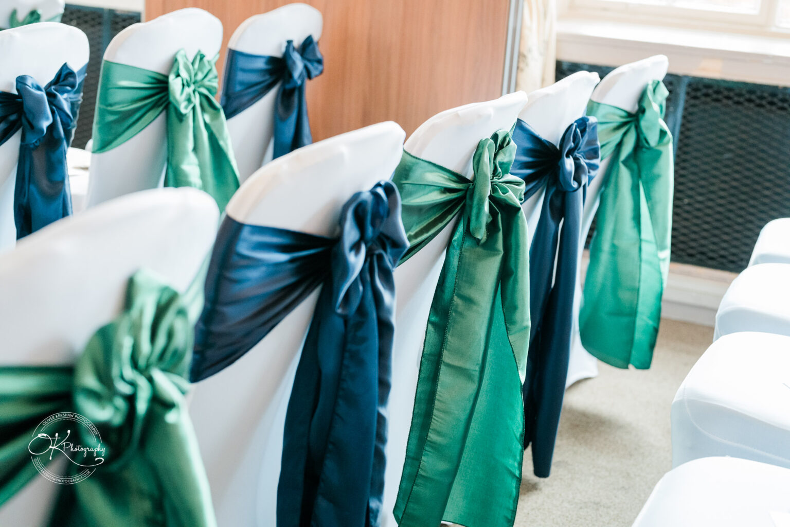 A row of white chairs adorned with alternating blue and green sashes in a conference setting.
