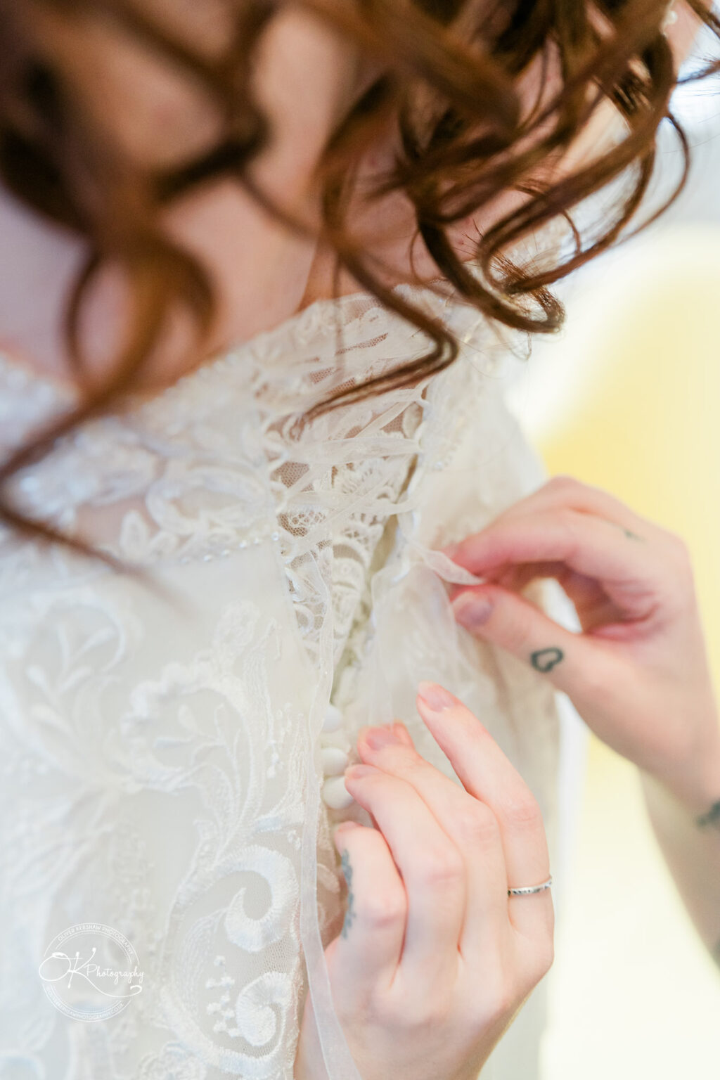 A person adjusting the intricate lace back of a wedding dress.