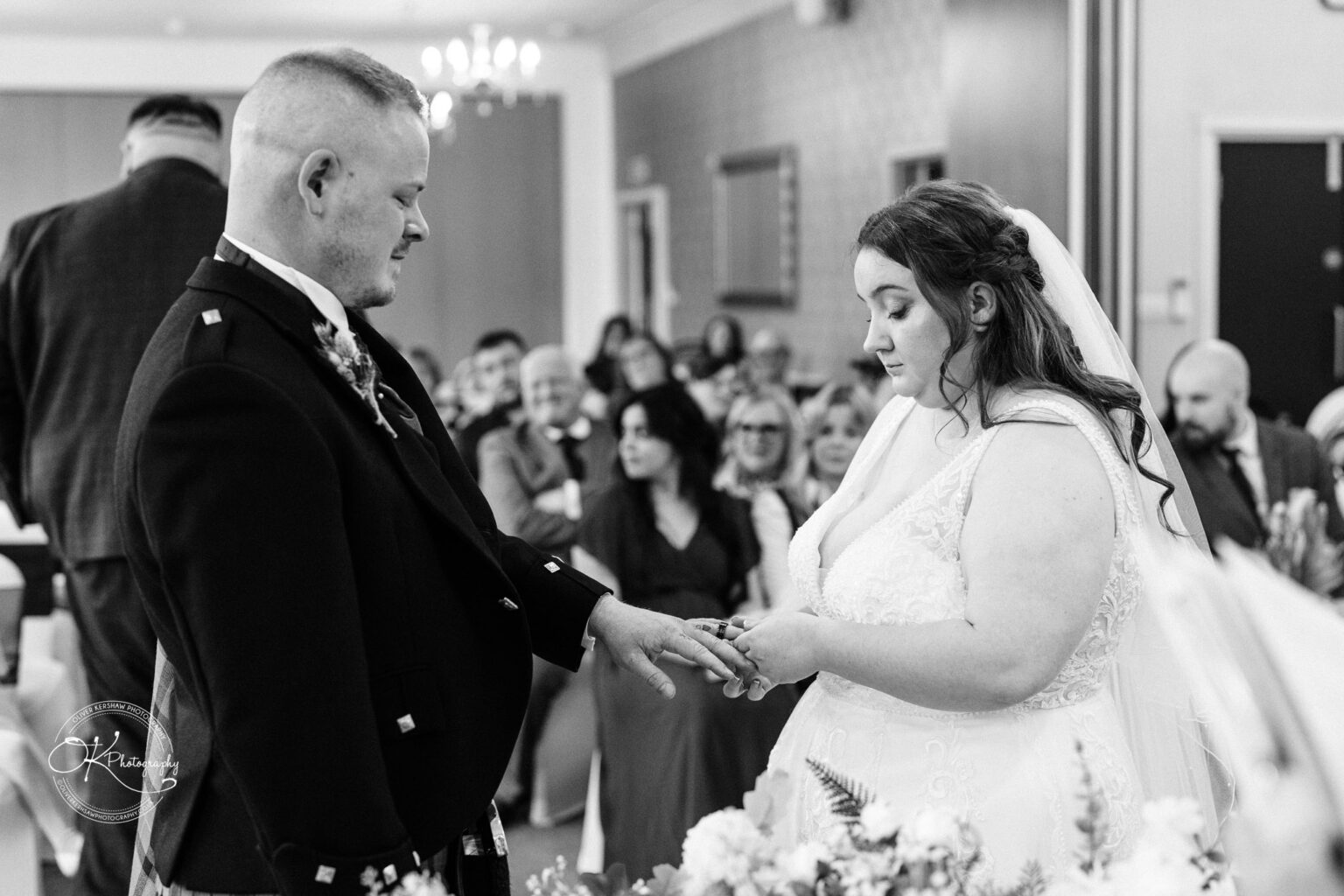 A couple exchanging rings during a wedding ceremony, with guests in the background.