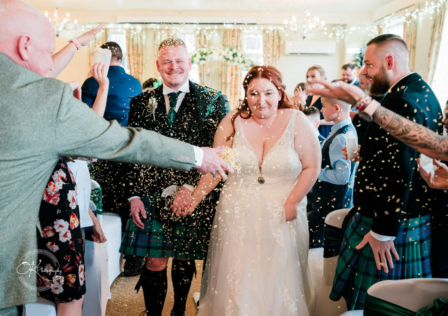 Bride and groom smiling while guests throw confetti, indoor wedding ceremony at Derby Conference Centre.