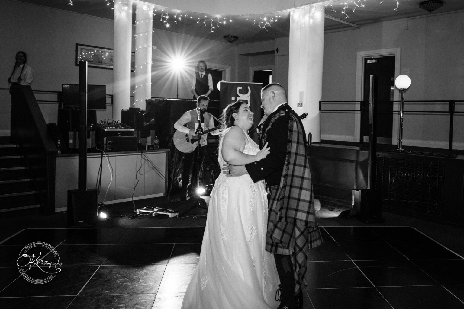 A bride and groom dance together at their wedding reception with a live band performing in the background.