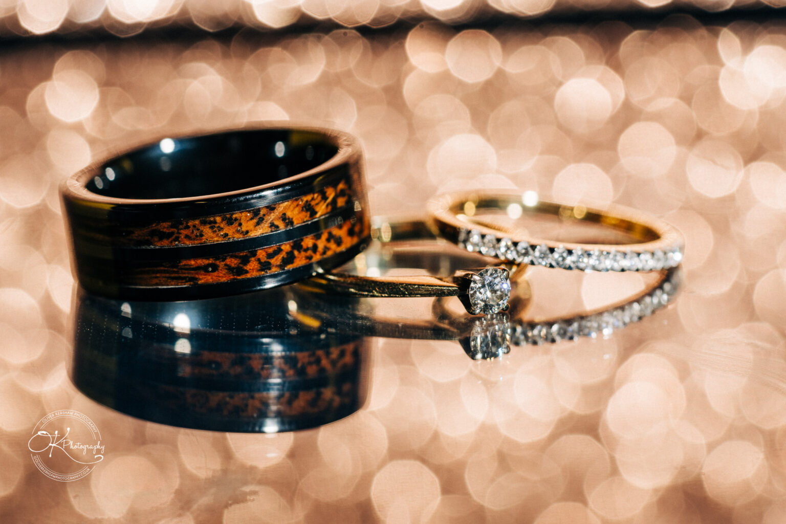 A close-up of wedding rings on a reflective surface with a bokeh background.