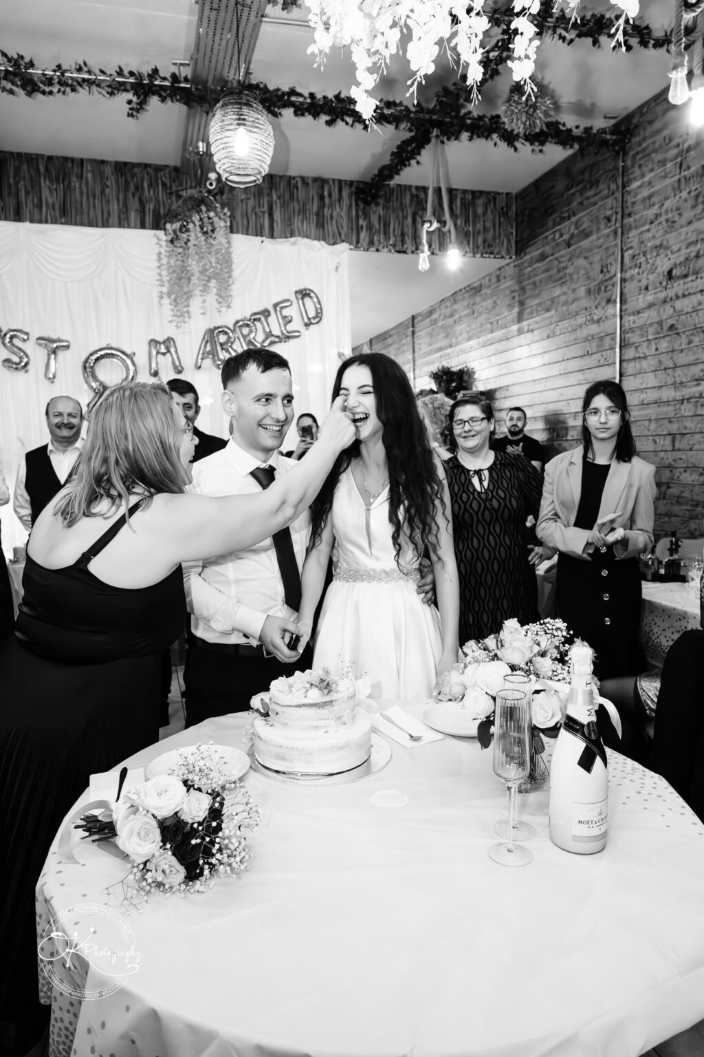 Konstandin and Bleona enjoying their wedding celebration with family and friends, laughing as a guest playfully feeds them cake.