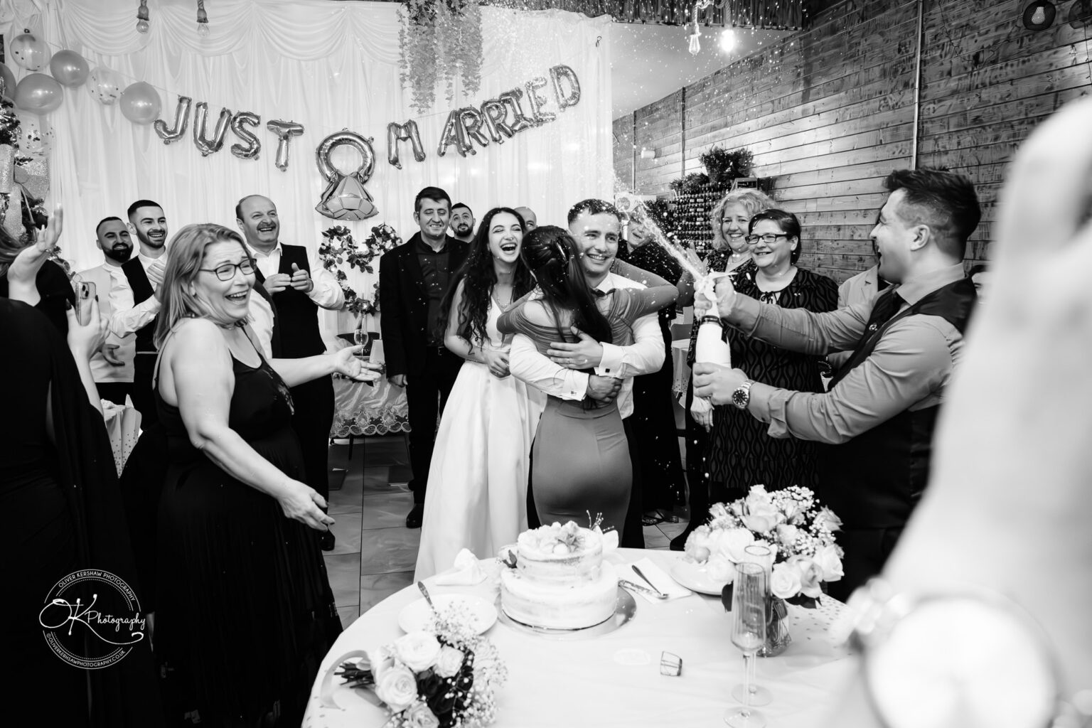 Konstandin and Bleona at their wedding, smiling and laughing as a guest feeds them cake, captured by Oliver Kershaw Photography.