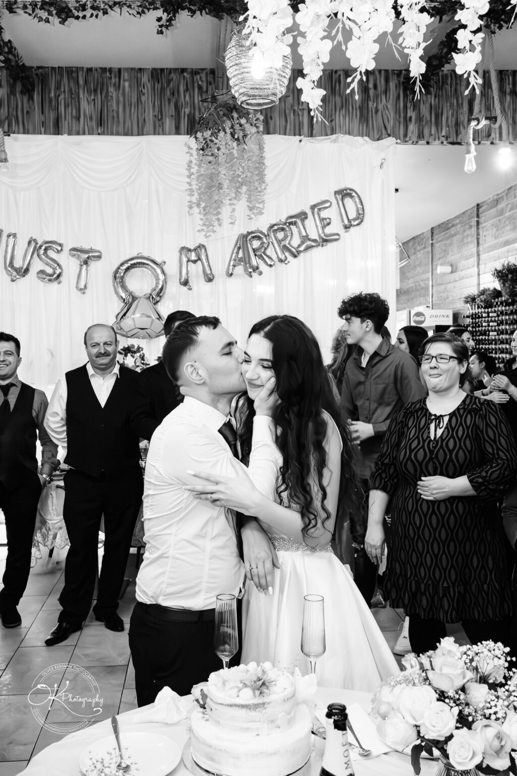 Konstandin and Bleona at their wedding reception, sharing a joyful moment with friends and family, captured by Oliver Kershaw Photography.