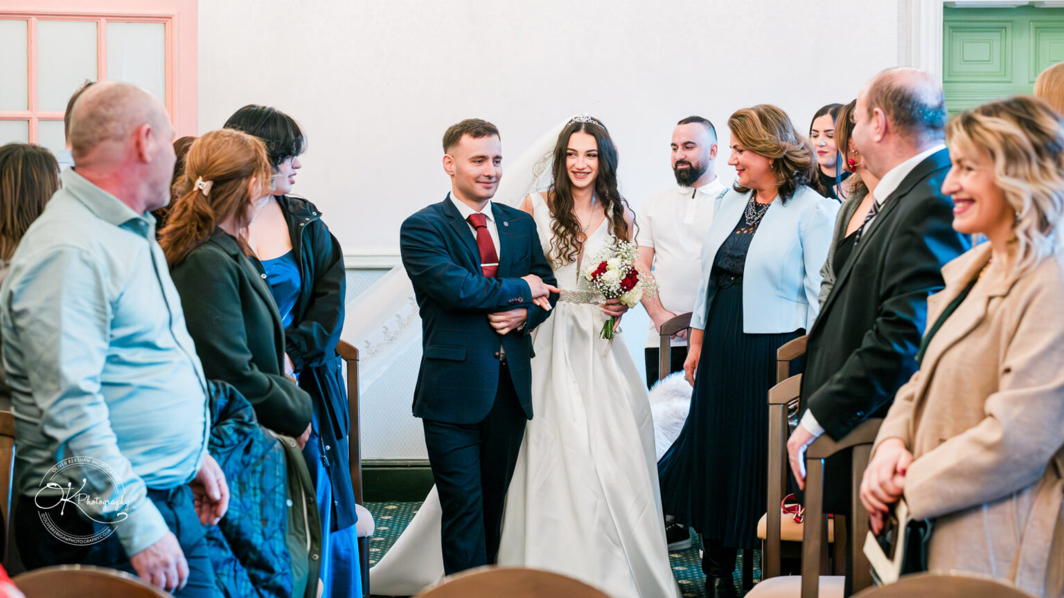 A bride and groom walk arm-in-arm down the aisle, smiling, as their guests look on joyfully.