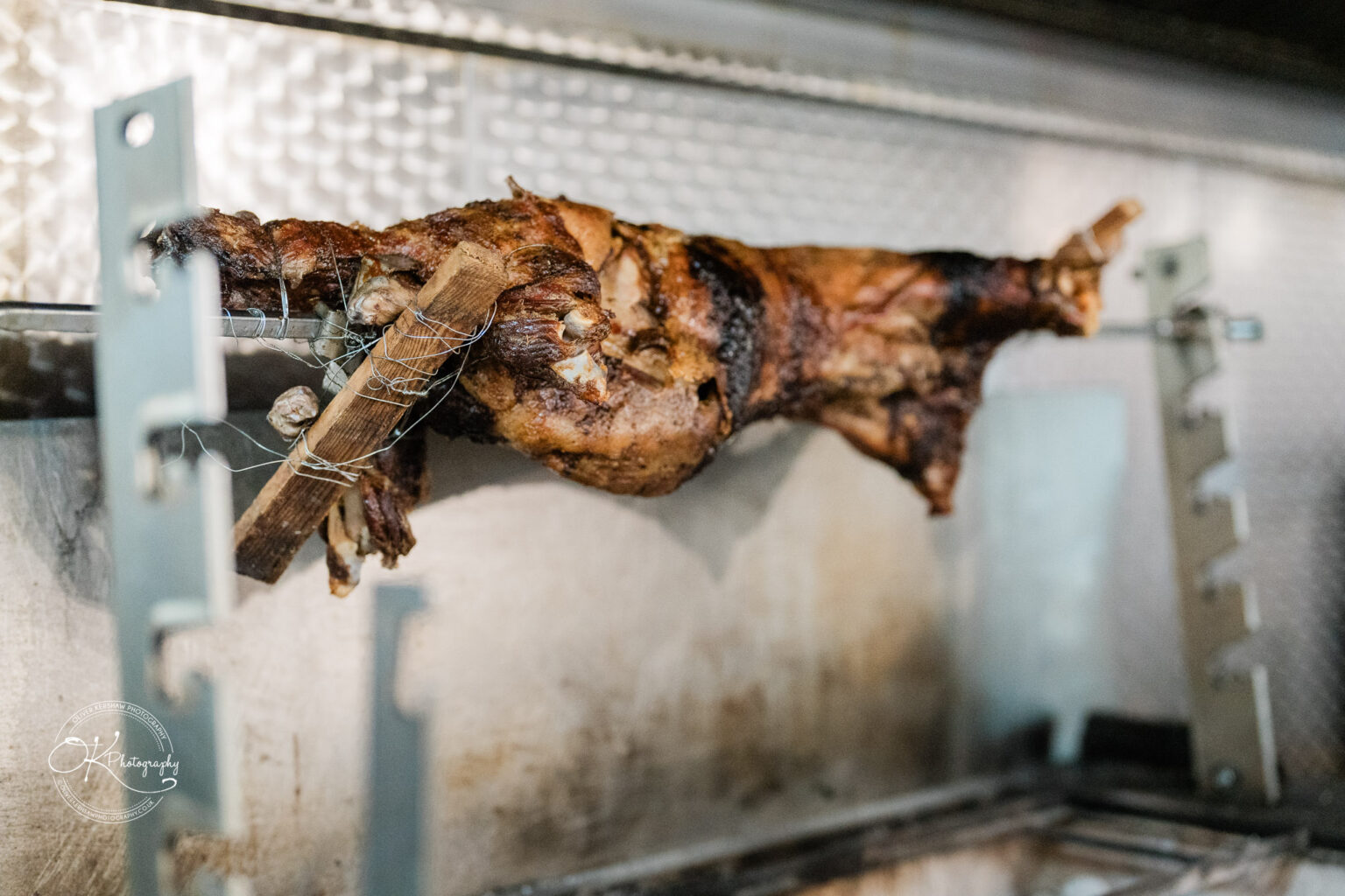 Roasted meat on a rotisserie spit inside a grill.