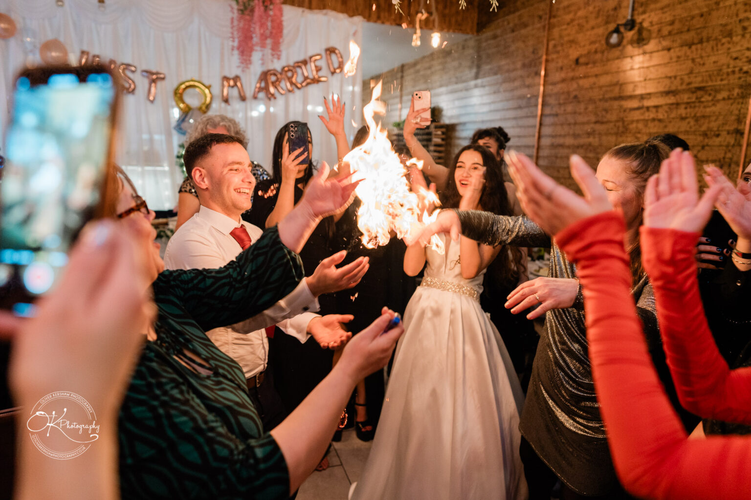 People celebrating at a wedding with a fire performance, with "Just Married" balloons in the background.