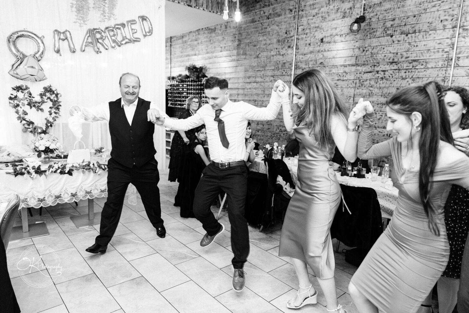 Group of people dancing in a wedding reception, with "Just Married" decorations in the background.