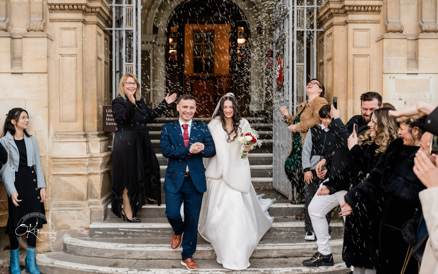 Bride and groom exiting a building while guests throw confetti at them.