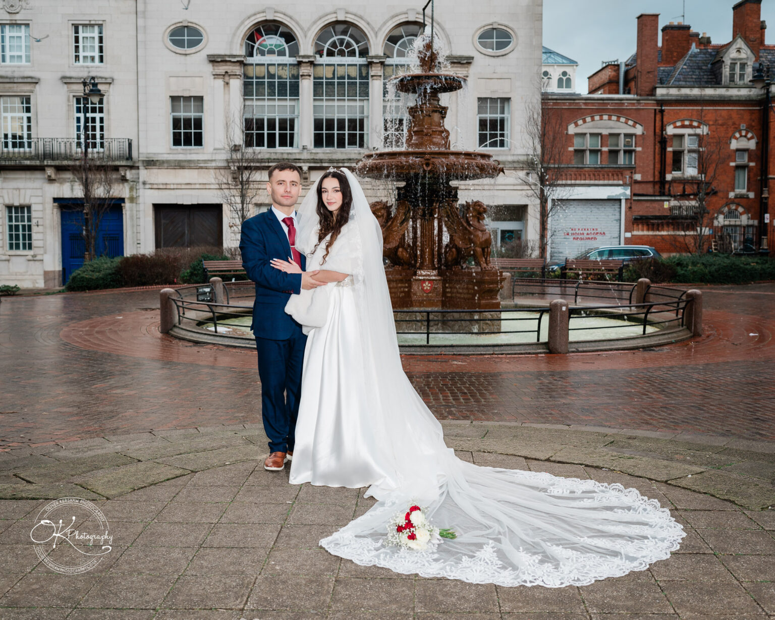 Bride and groom posing in front of a fountain and historic buildings.