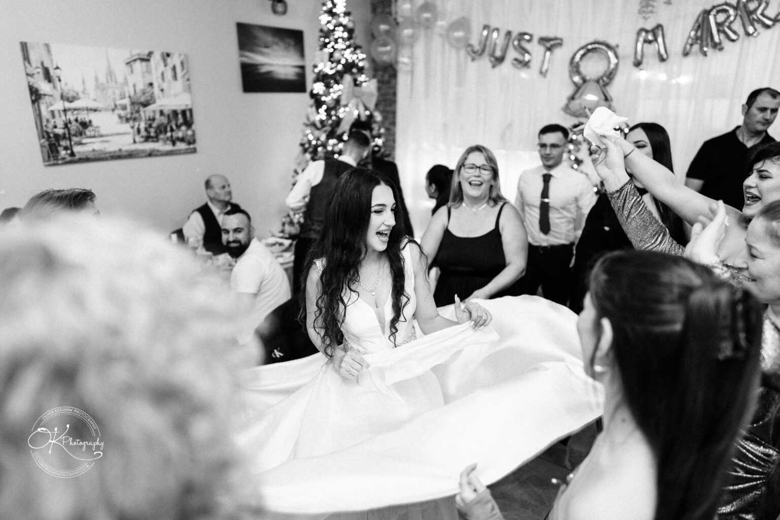 Bride dancing joyfully with guests around her at a wedding reception, with "Just Married" balloons in the background.