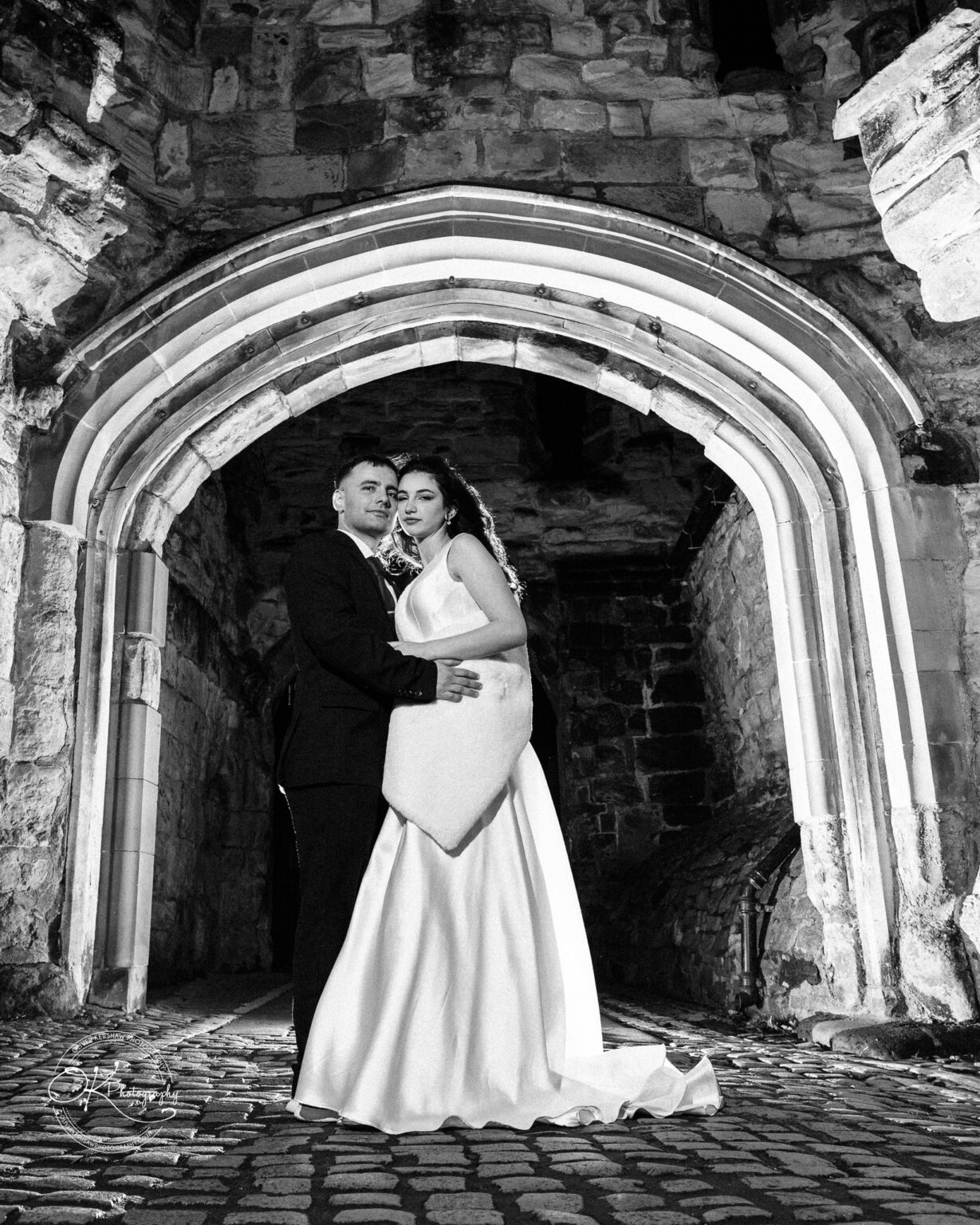 Konstandin and Bleona at their wedding celebration, smiling as a guest feeds them cake, captured by Oliver Kershaw Photography.