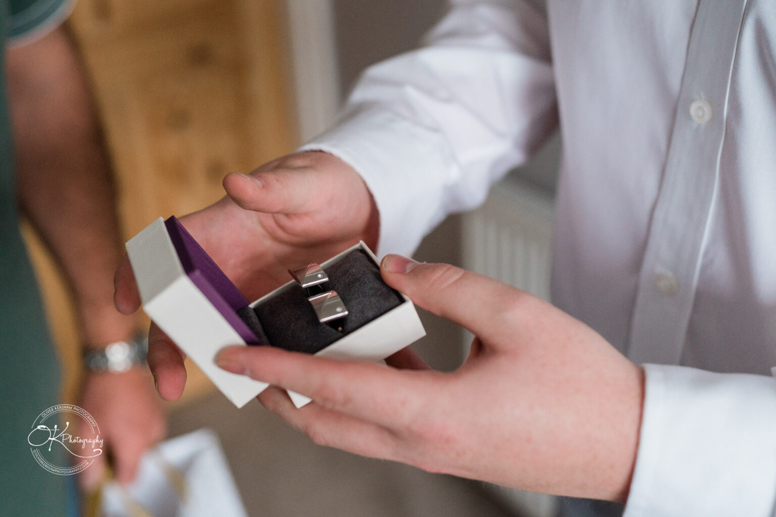 A person holding an open box containing cufflinks, dressed in a white shirt.