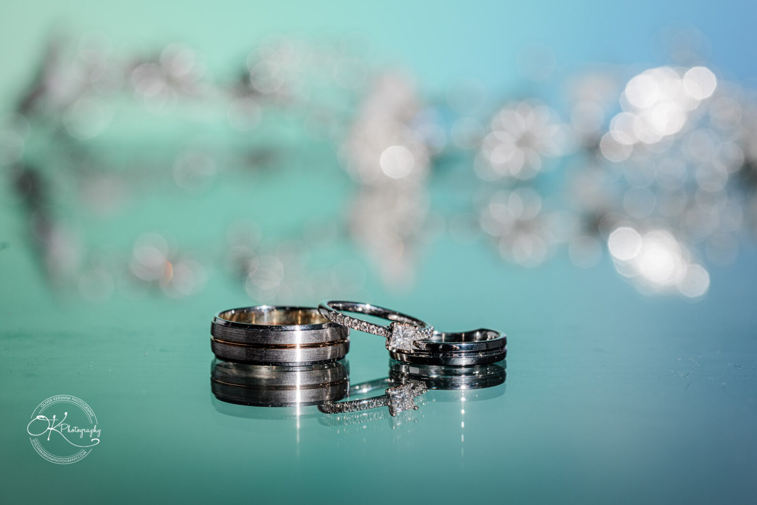 A close-up of wedding rings placed on a reflective surface with a colorful, blurred background.