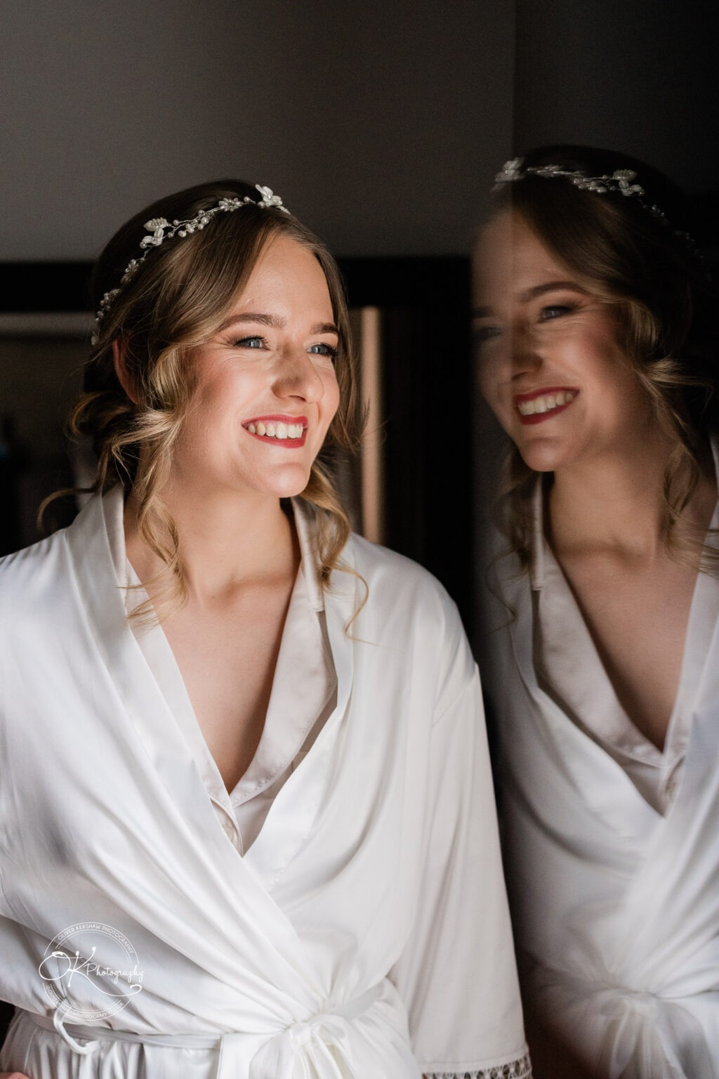 A bride smiling brightly while looking out of a window, her reflection visible in the glass.
