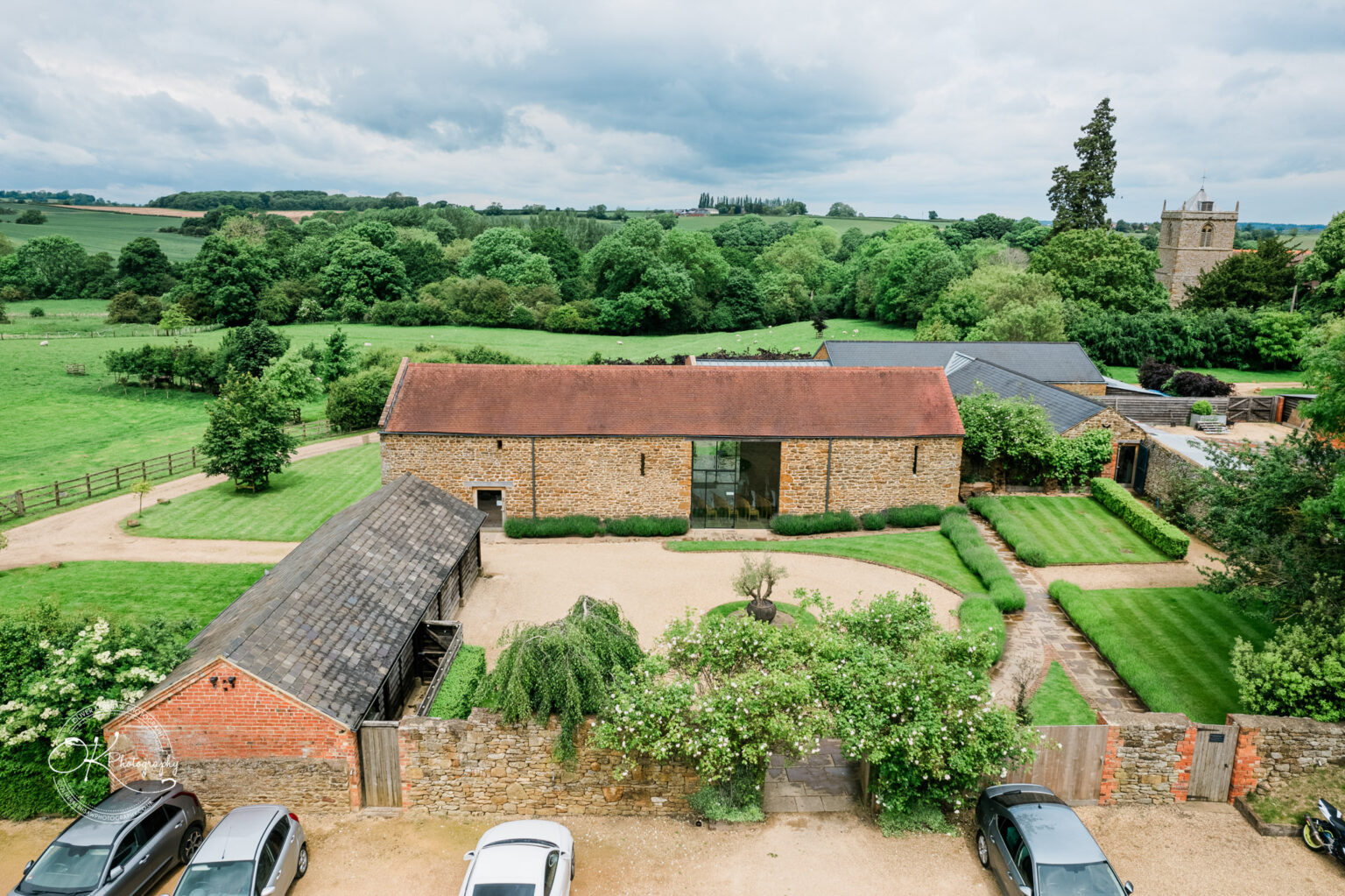 A wide view of the Dodford Manor venue, showcasing its beautiful green surroundings and rustic buildings.