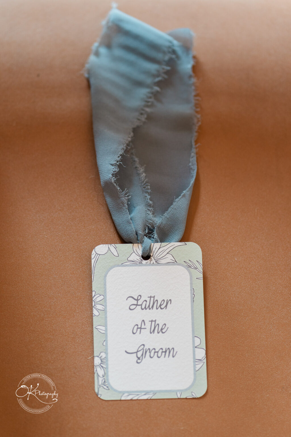 A close-up of a Father of the Groom tag attached to a light blue ribbon.