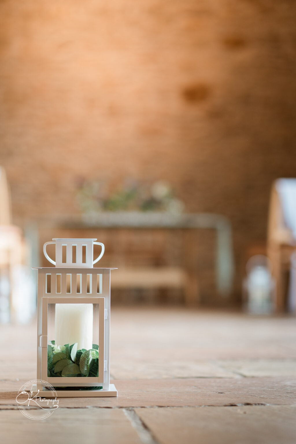 A white decorative lantern placed on a brick floor, with a blurred background of a wedding venue.