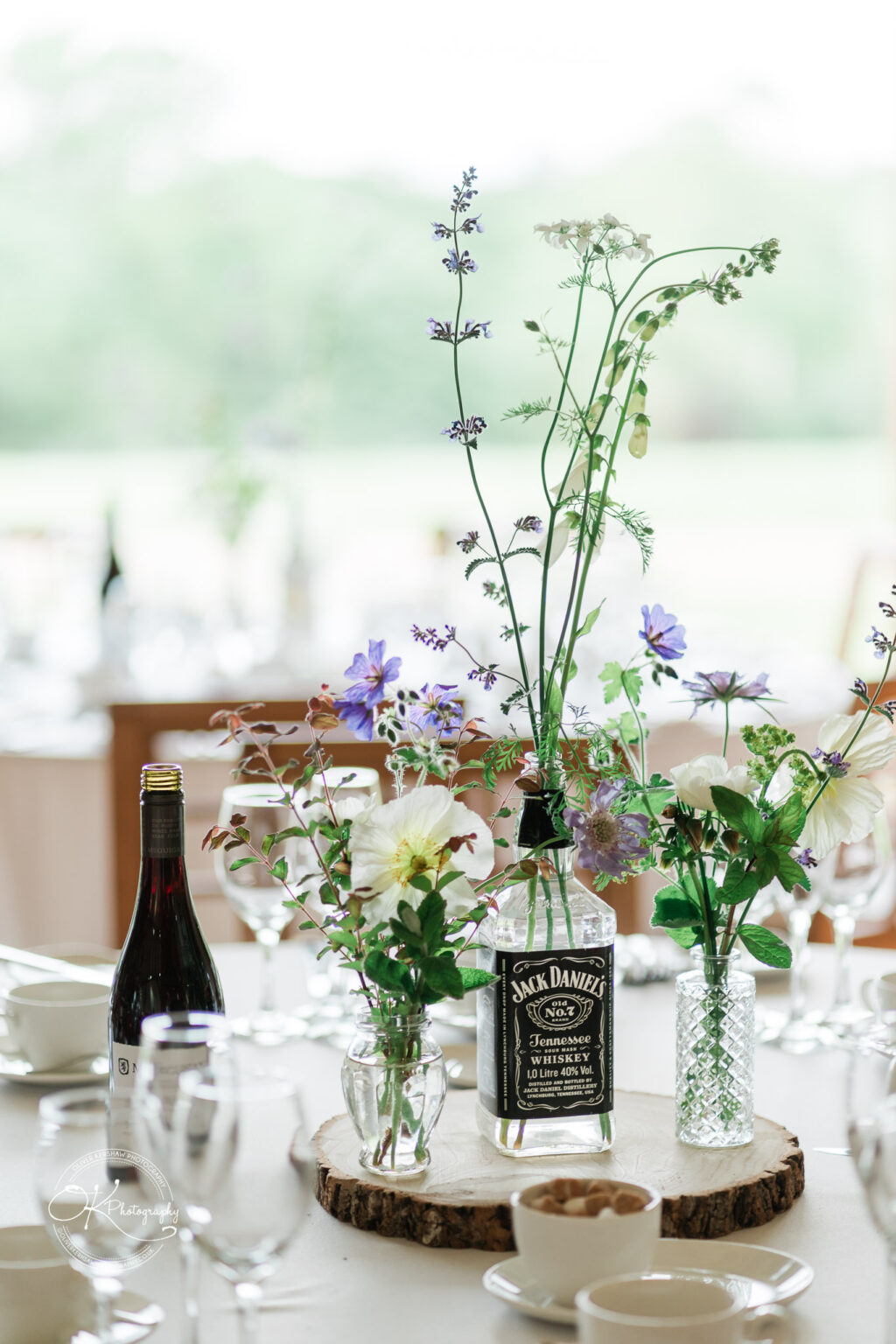 A table centerpiece made from a Jack Daniel's bottle filled with wildflowers, set among other decor.