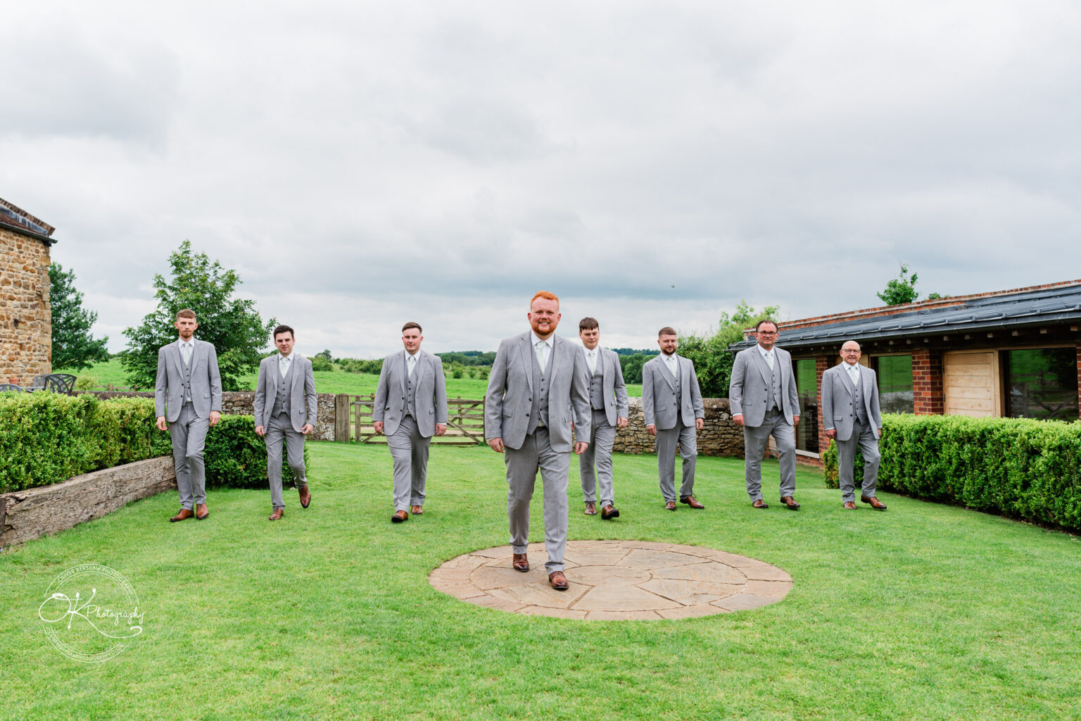 Groomsmen dressed in grey suits walking towards the camera, led by the groom.