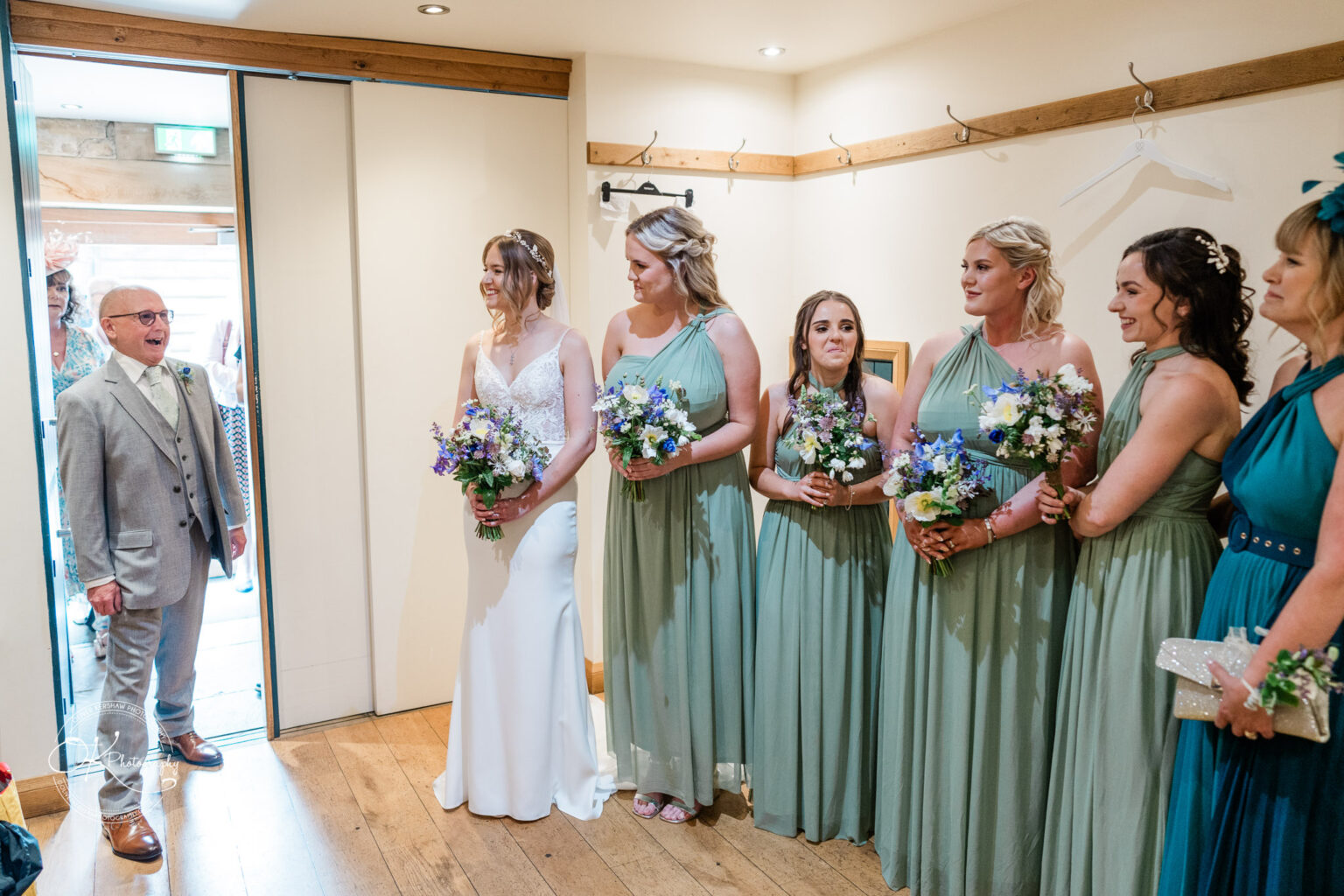 The bride and her bridesmaids reacting with smiles as they see the father of the bride for the first time in the doorway.