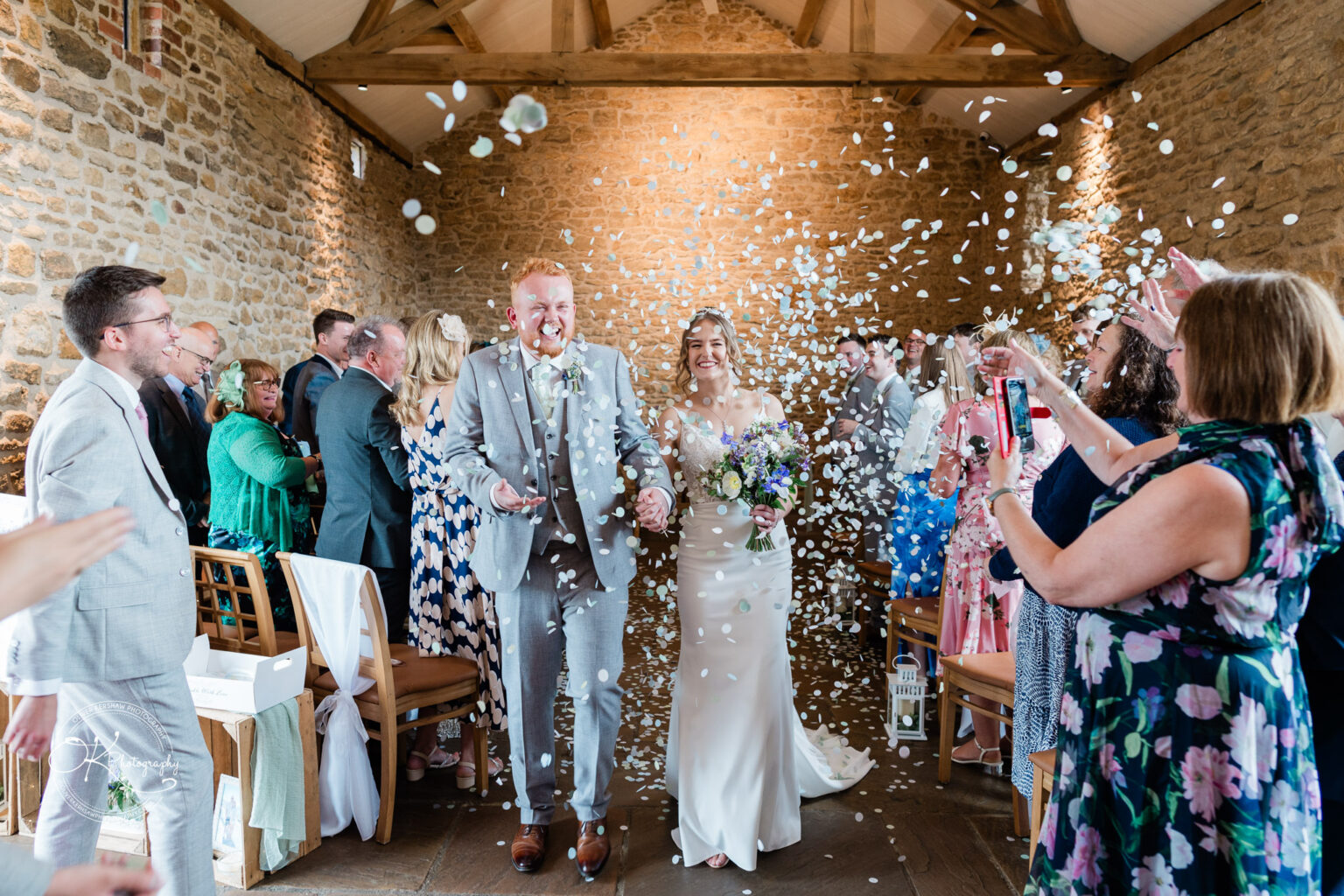 Bride and groom walking down the aisle with confetti at Dodford Manor