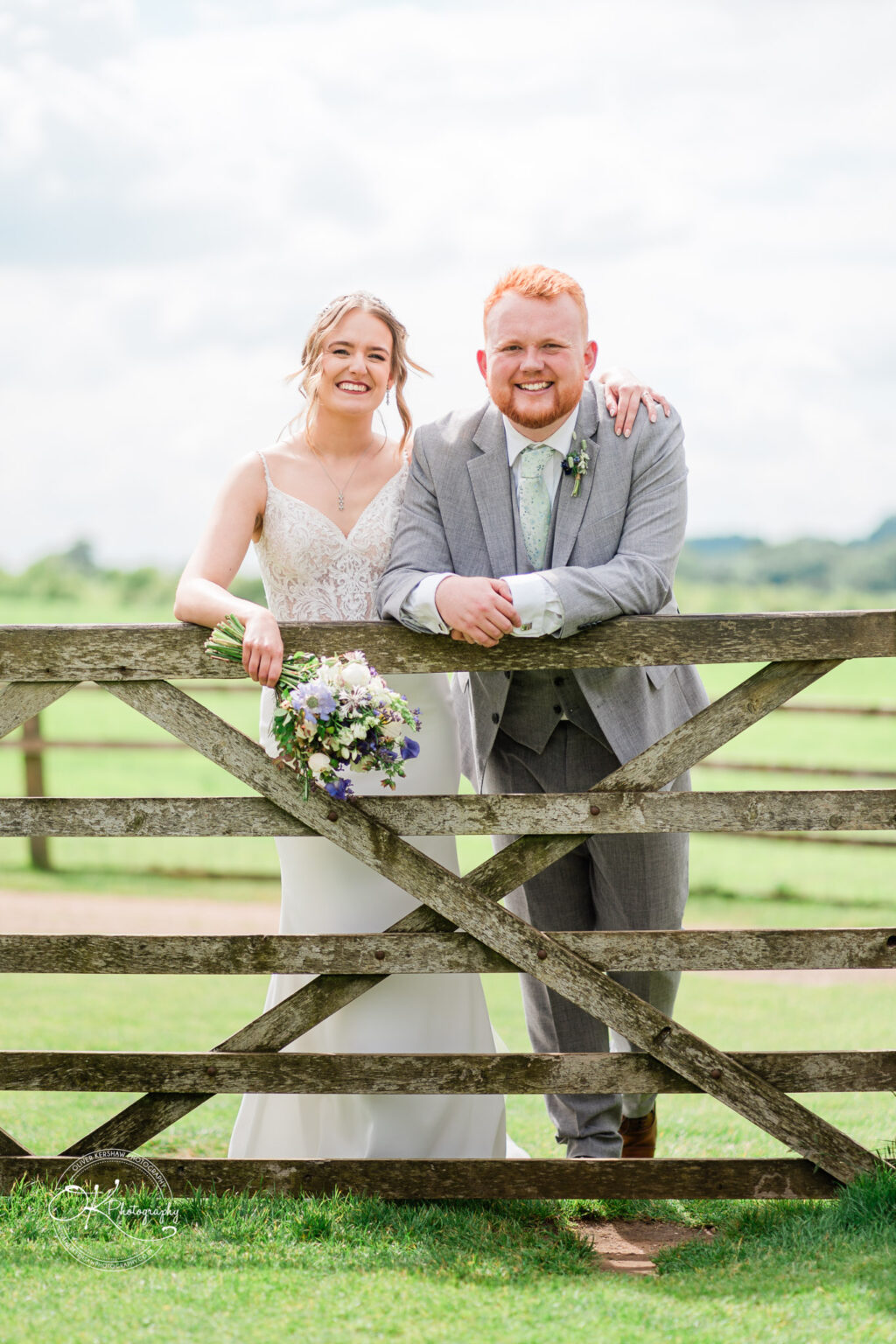 Bride and groom leaning on a rustic wooden gate at Dodford Manor