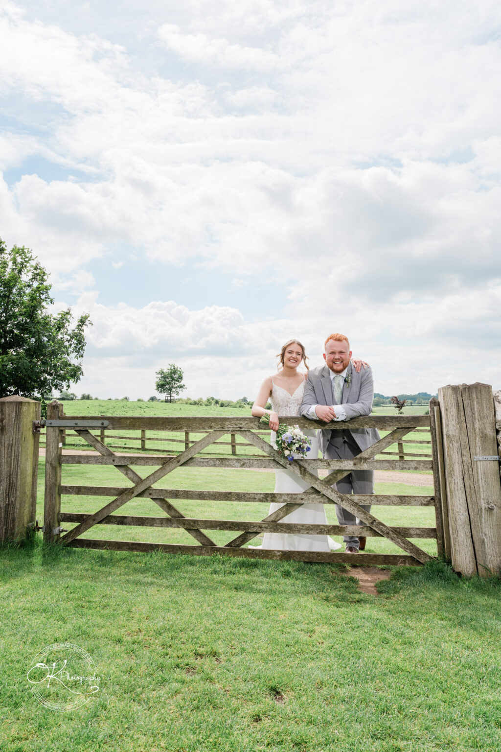 Bride and groom smiling at the camera by a wooden gate at Dodford Manor