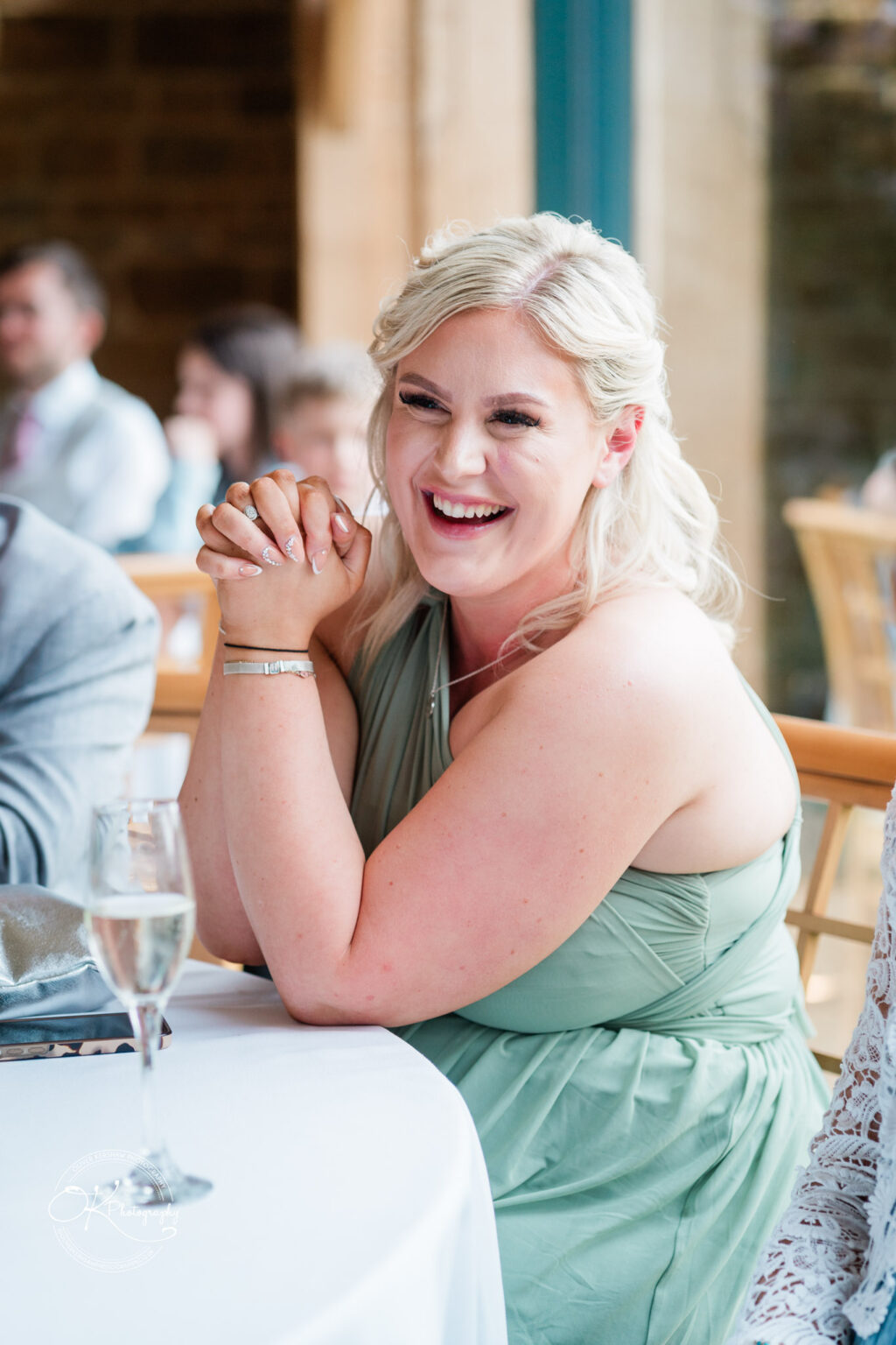 A blonde woman in a green bridesmaid dress smiling and enjoying a speech during a wedding reception at Dodford Manor.