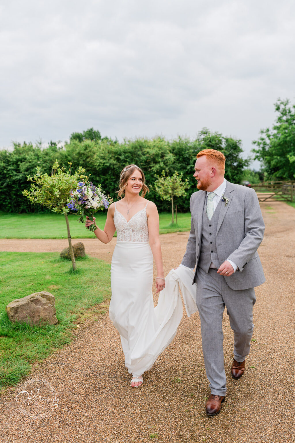 The bride and groom walk hand in hand, smiling and chatting, during their wedding at Dodford Manor.