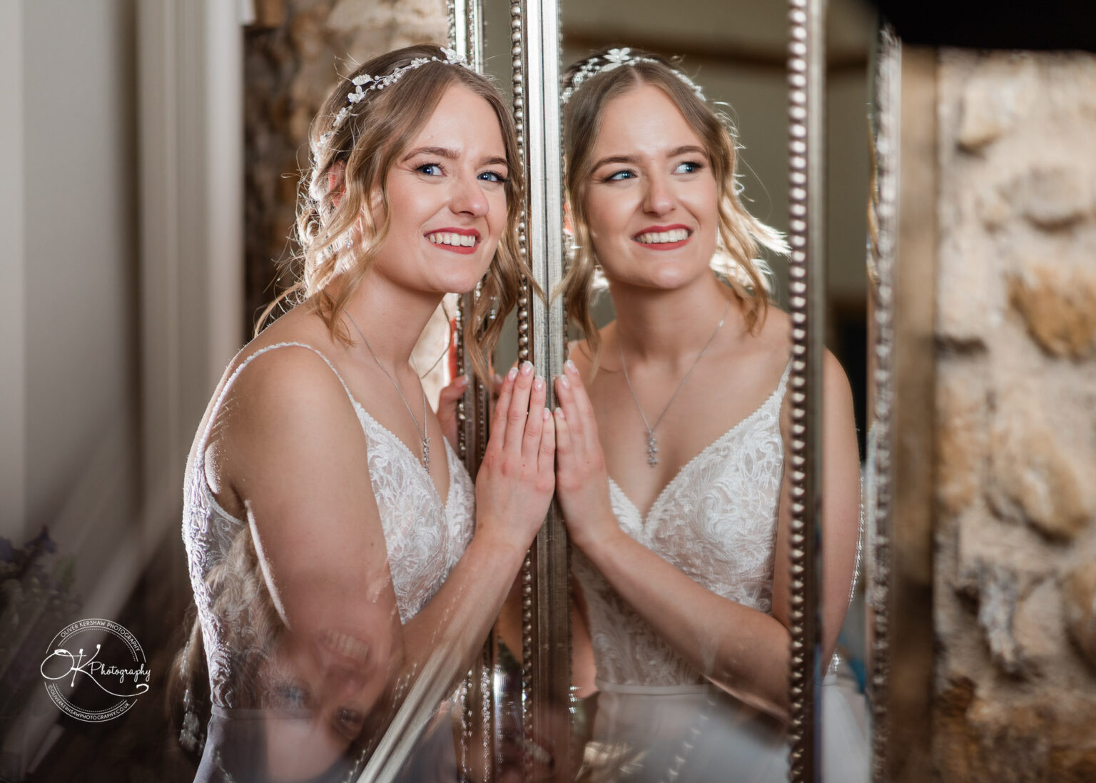 The bride smiling while looking into a mirror, creating a reflection effect, at Dodford Manor.