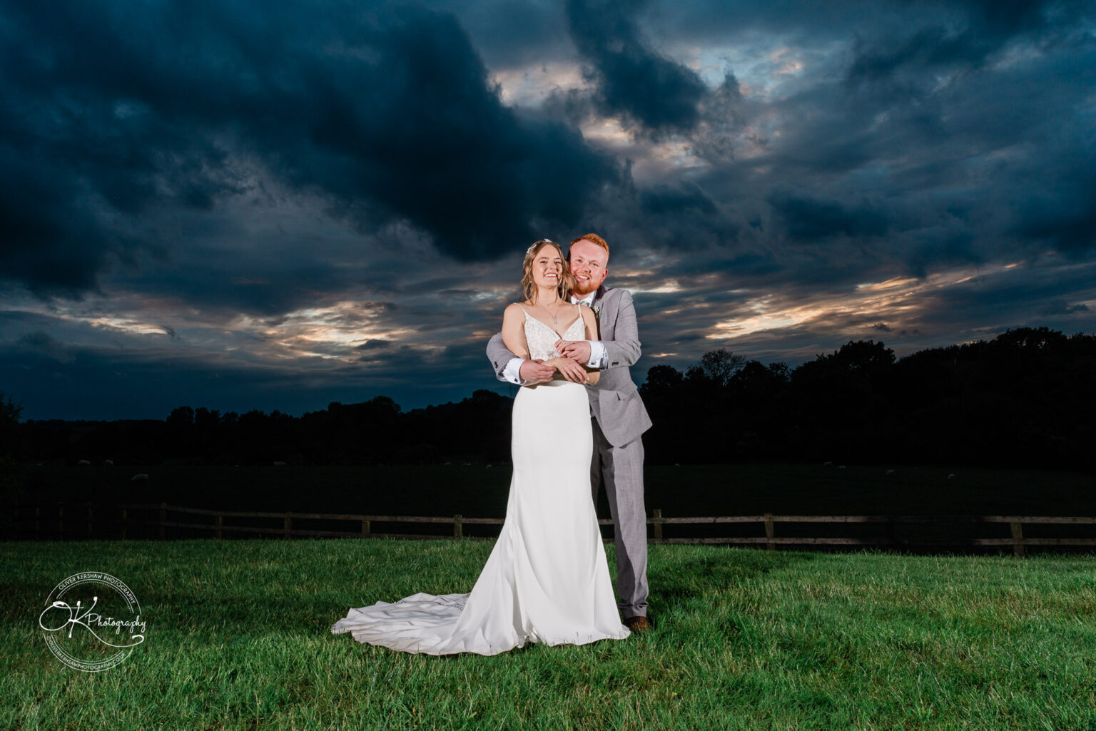 The bride and groom embrace each other with a dramatic evening sky in the background at Dodford Manor.