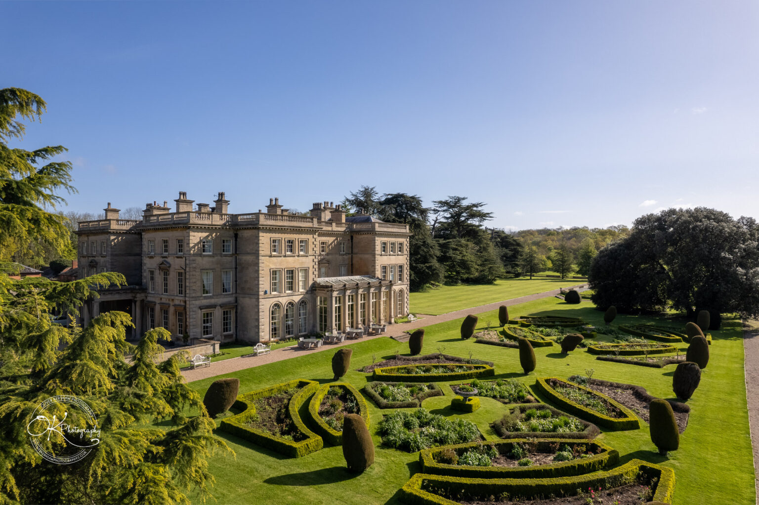 Aerial view of Prestwold Hall, a historic English manor surrounded by manicured gardens and expansive green lawns on a sunny day.