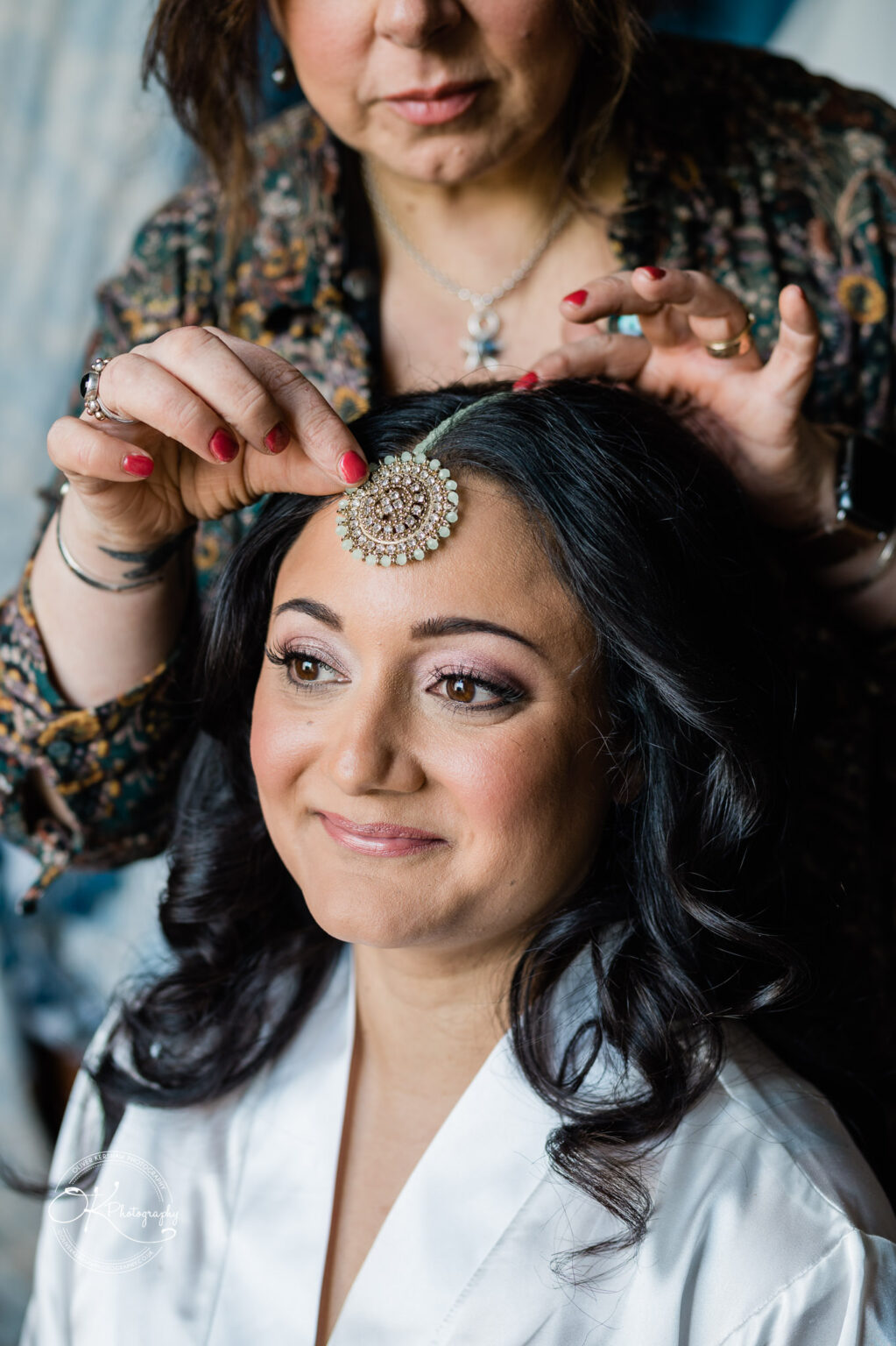 Close-up of a bride smiling as a headpiece is gently placed on her forehead.