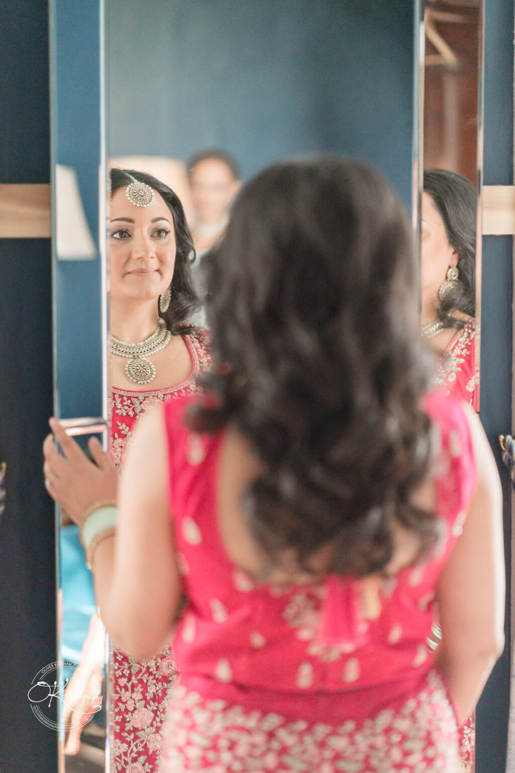 Bride looking at herself in the mirror, adorned in traditional red bridal attire with jewelry.