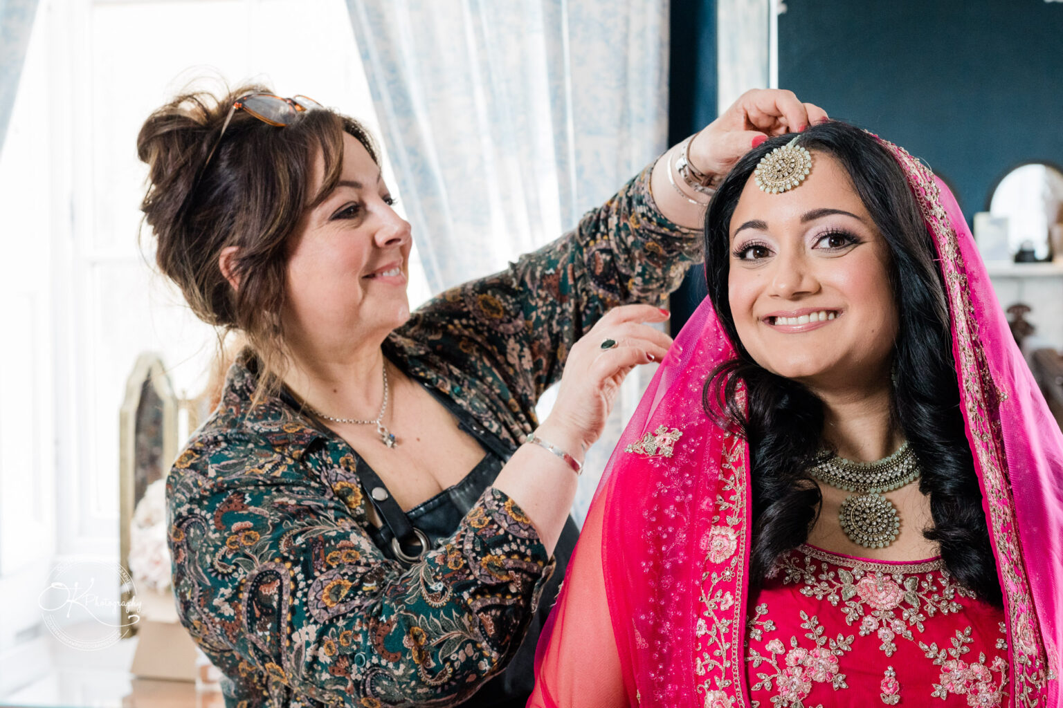 Bride smiling as she gets her headpiece adjusted by a woman during wedding preparations.