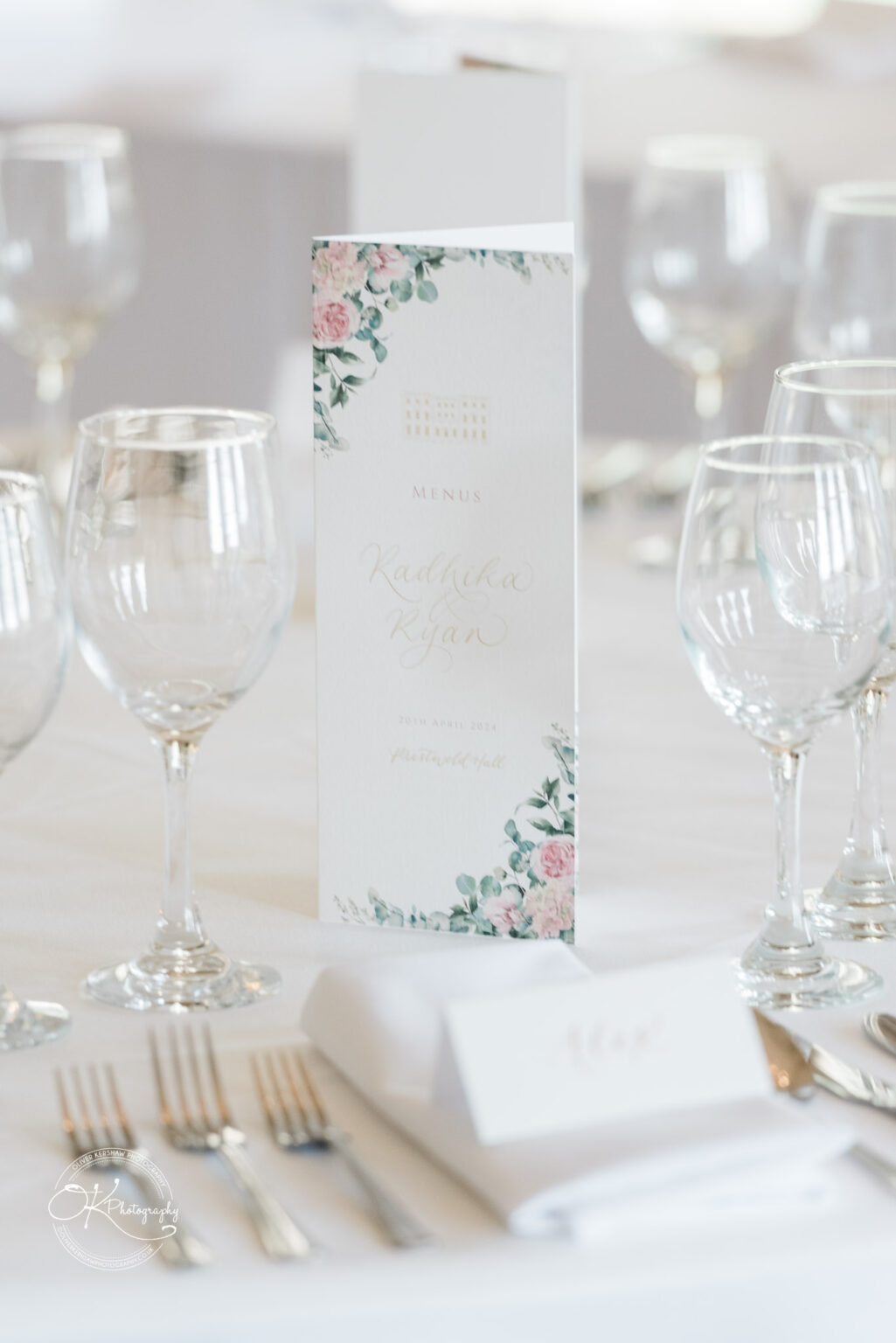 Elegant table setting with floral-themed wedding menu, wine glasses, and cutlery.