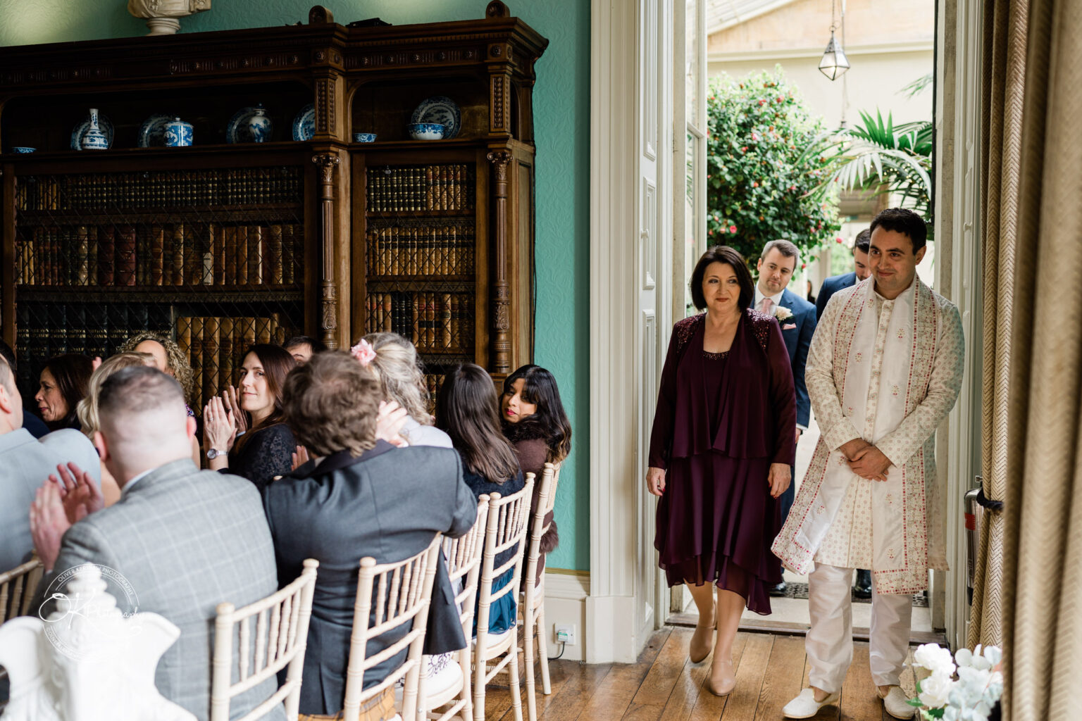 Groom entering the wedding venue accompanied by his family as guests look on.