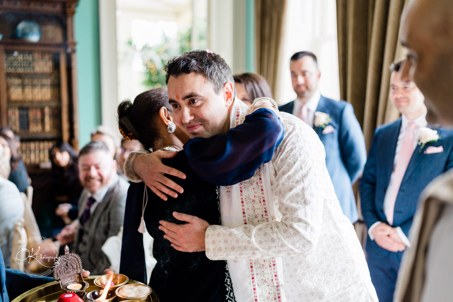 Groom warmly embracing an elder during the wedding ceremony, surrounded by guests.