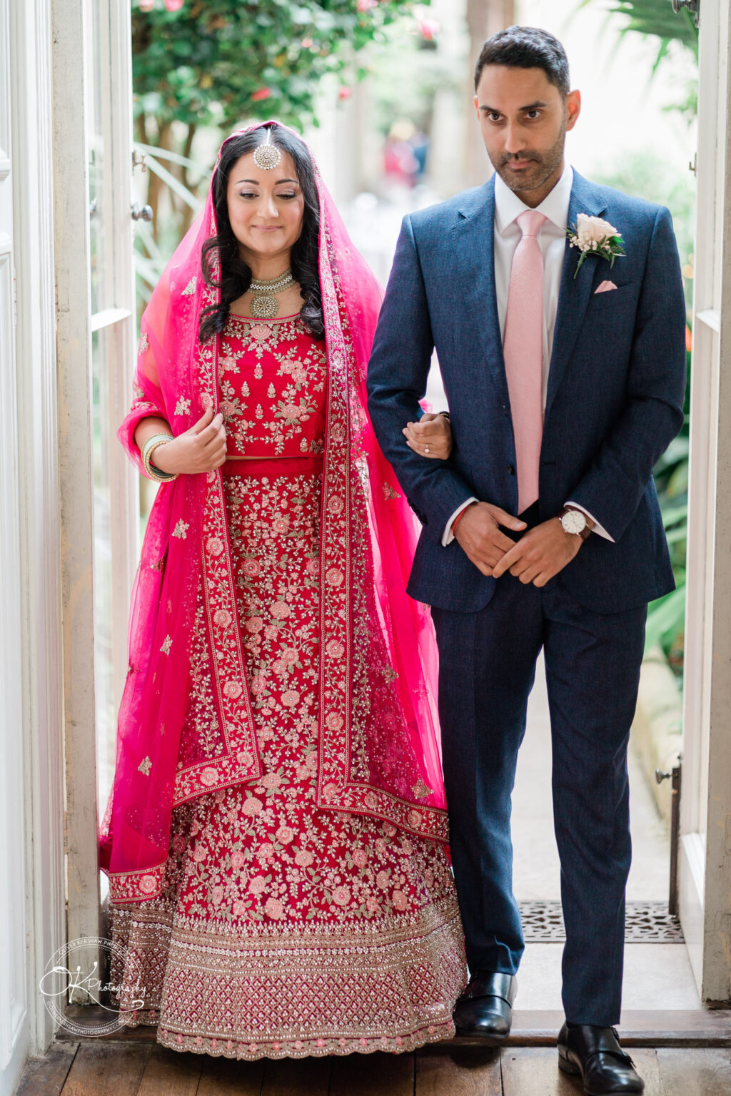 Bride in vibrant red attire walking down the aisle with a groomsman during the wedding ceremony.