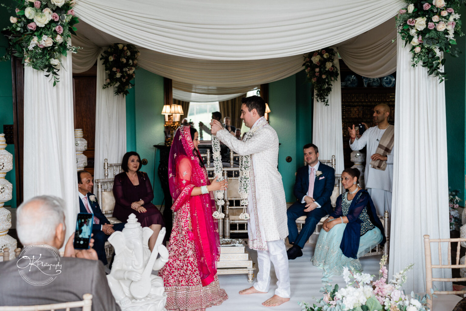 Bride and groom exchanging garlands under a floral canopy during their wedding ceremony.