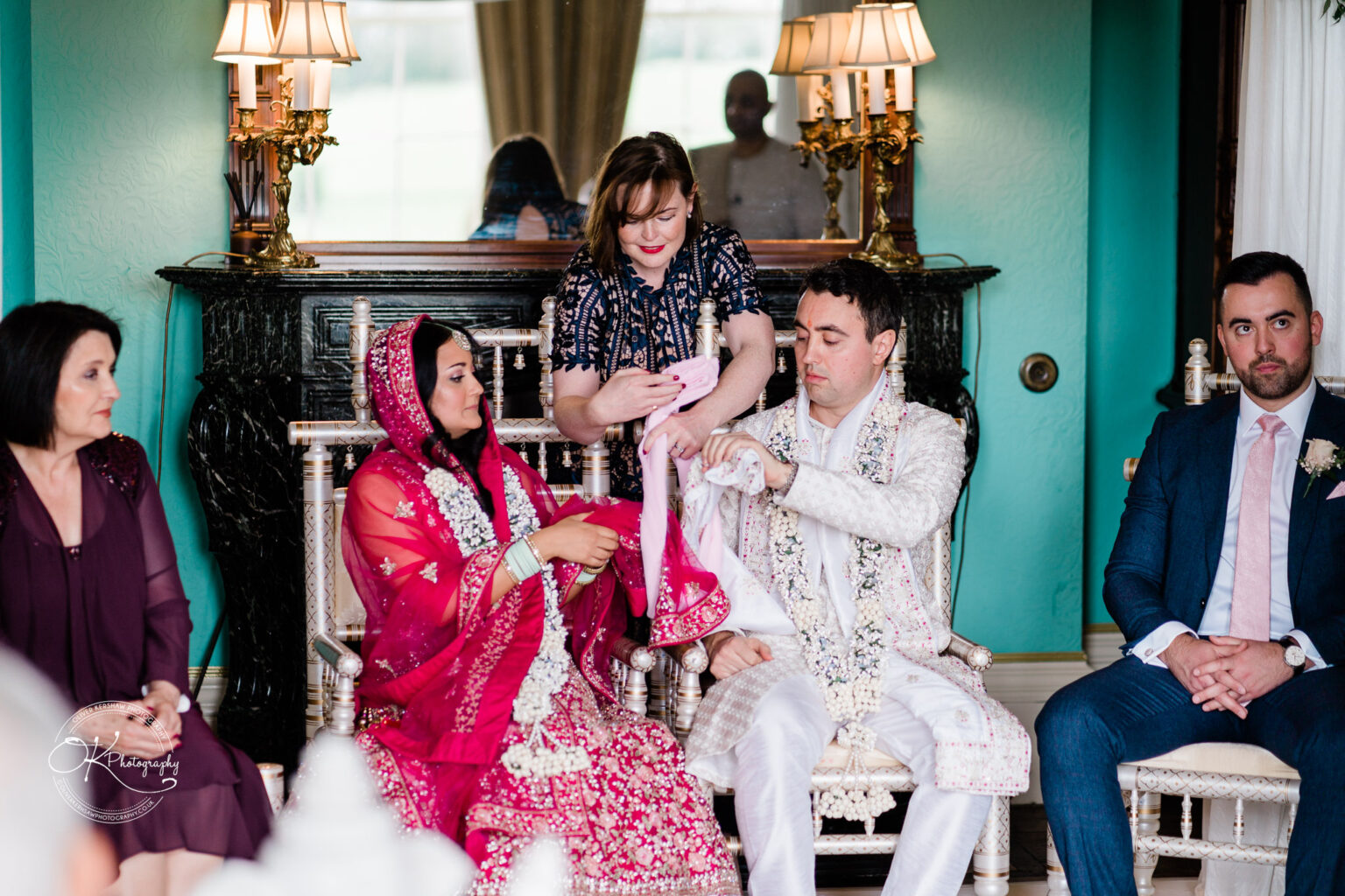 Wedding officiant tying the couple's garments together as part of the Hindu ceremony, with family observing.